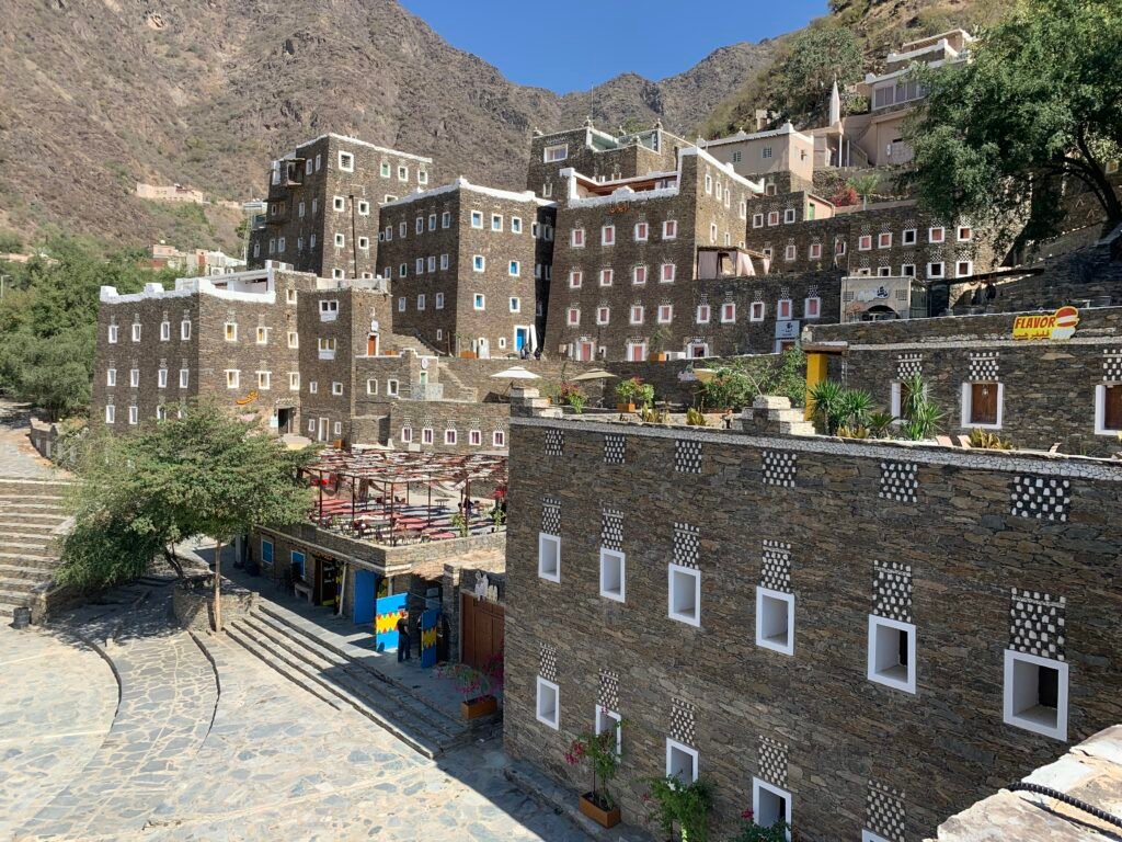 White window frames, white stones against brown rocks lined with white clay at the top of the Rijal Alma'a Museum. The museum itself occupies only the leftmost cube where the rest are actual dwellings.