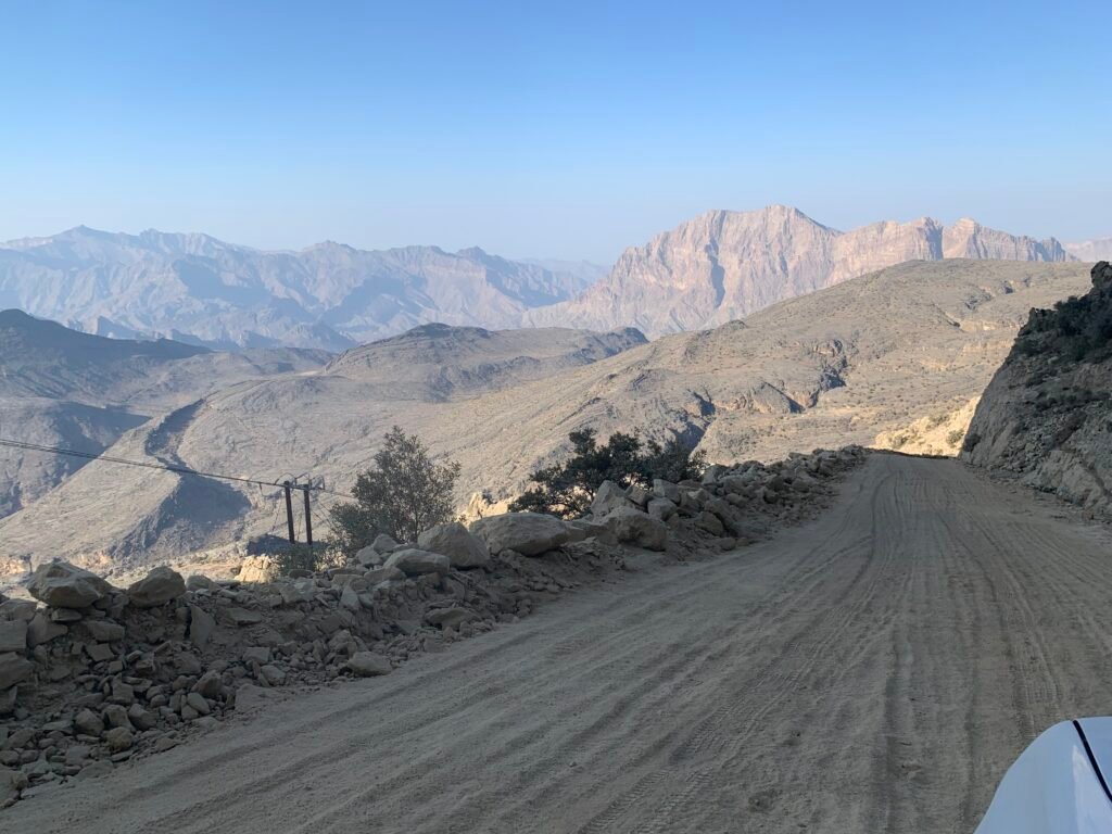 The unpaved road downhill against the backdrop of the Al Hajar Mountains